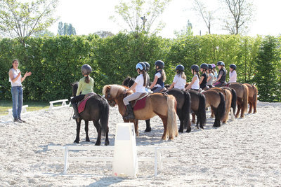 Une monitrice d'équitation, avec un groupe d'enfants, chacun sur un poney.