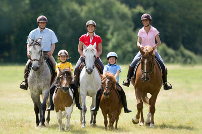 5 personnes sur la photo, dont 3 adultes, chacun sur un cheval, et 2 enfants sur des poneys.